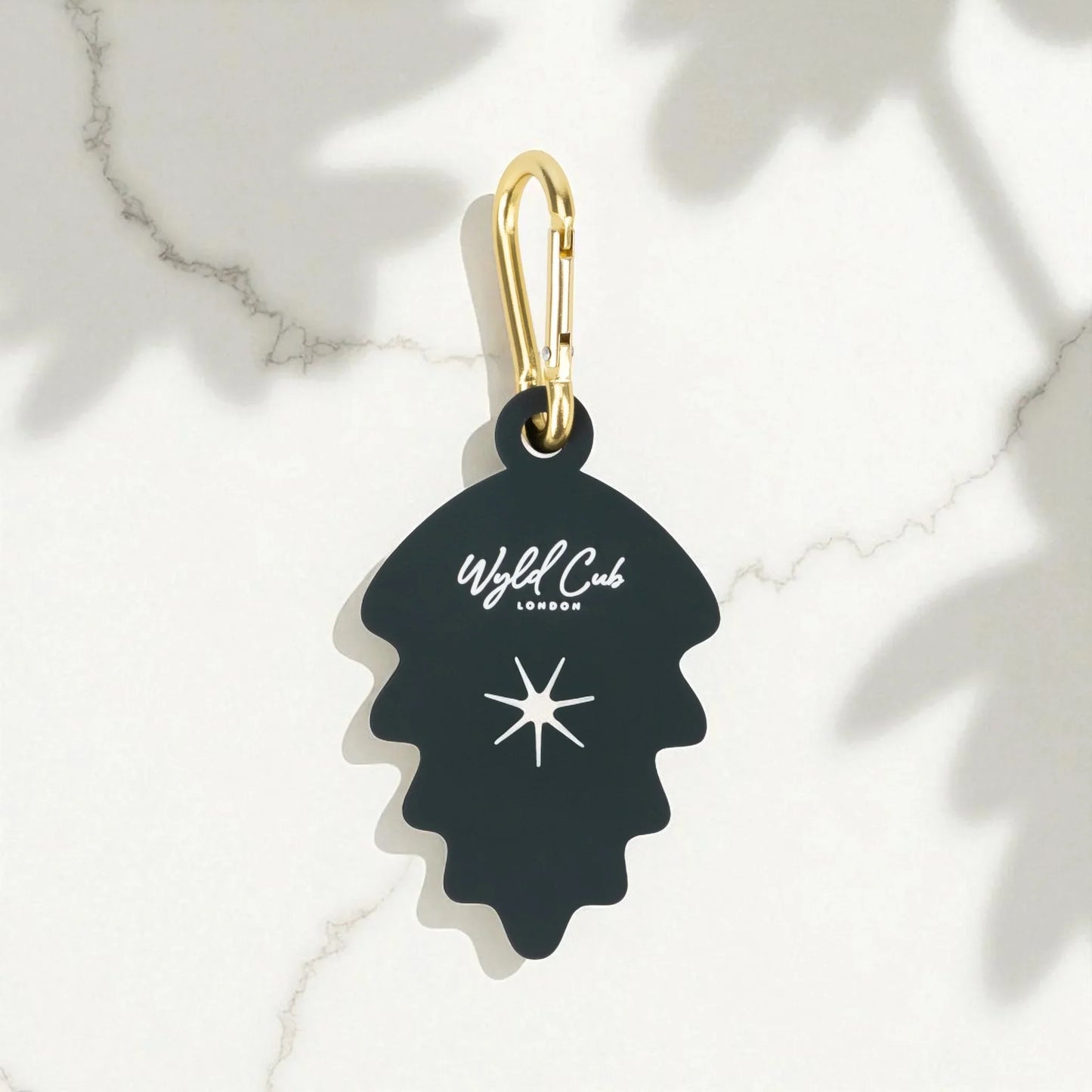 Black leaf-shaped keychain with white star and Wyld Cub London logo, gold metal clip on marble surface