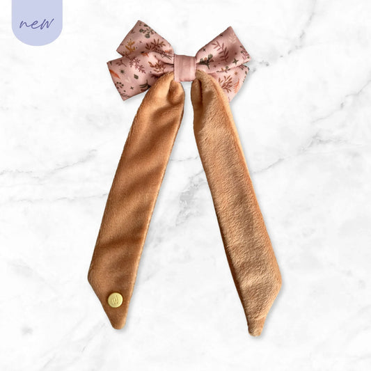 New pink floral fabric bow with long tan velvet tails on white marble background